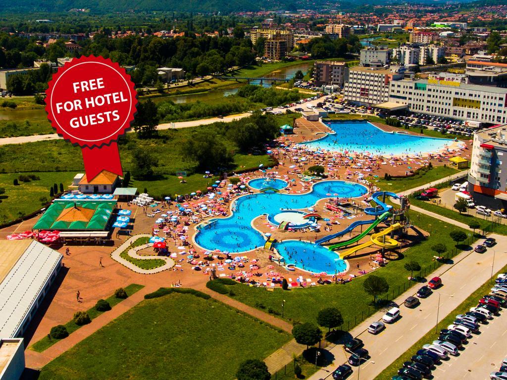 Hotel Hills Sarajevo Congress & Thermal Spa Resort Exterior photo The photo shows an aerial view of a large swimming pool area, likely part of a hotel or resort. There are several pools of different shapes and sizes, including one that resembles a Mickey Mouse shape. The area is filled with numerous sun loungers an